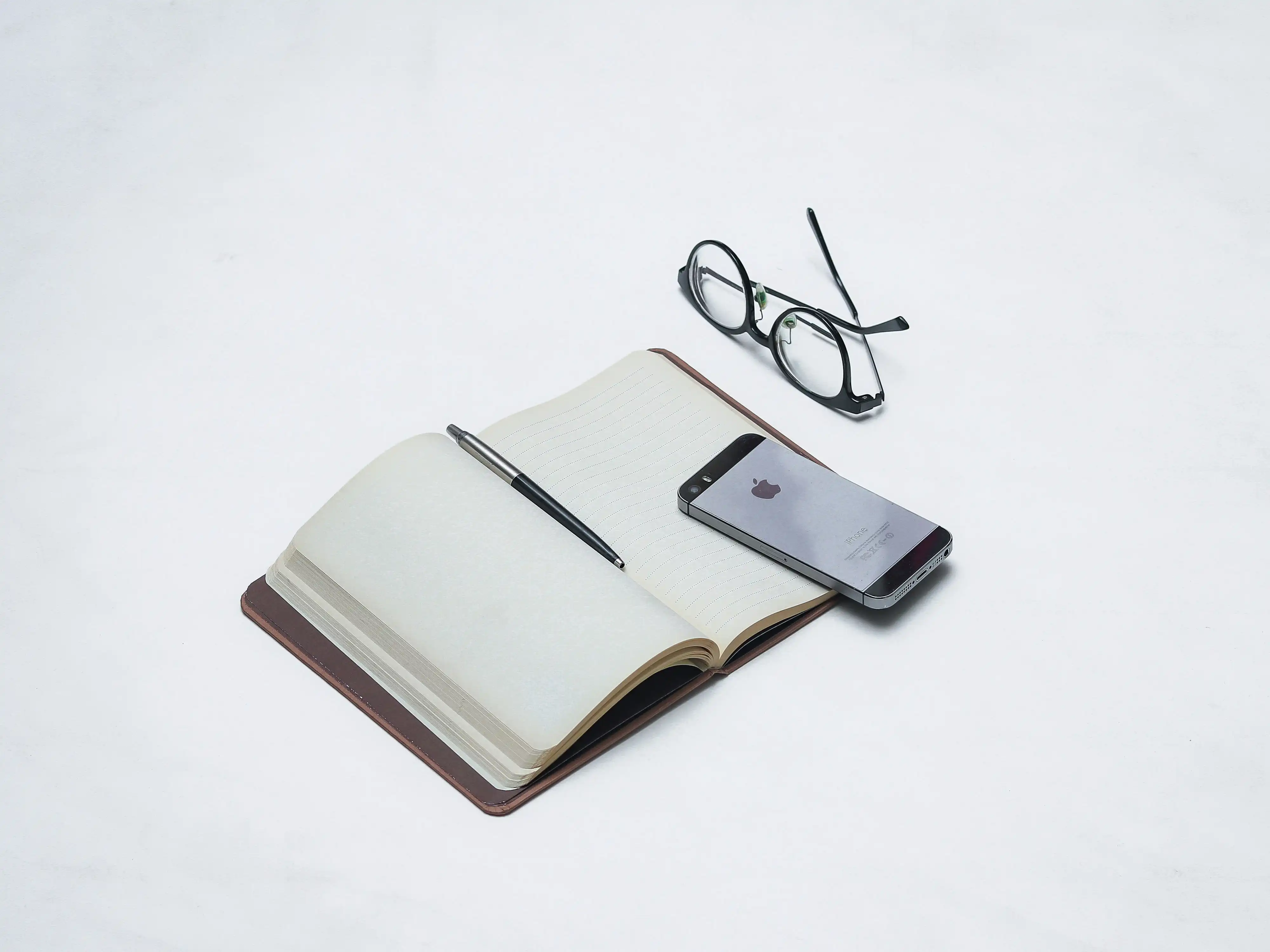 Person tracking habits in a journal with a smartphone nearby showing a habit tracking app